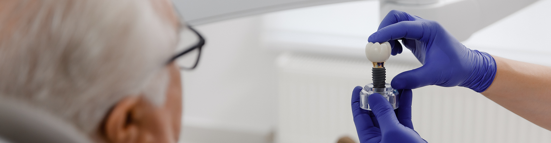 gloved hands holding implant model in front of man